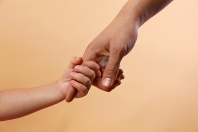 Photo of Father and child holding hands on beige background, closeup