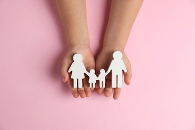 Photo of Child holding figure of family on light pink background, top view