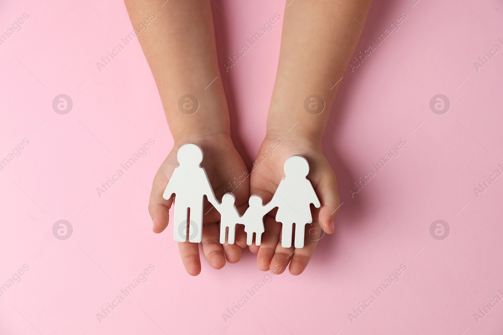 Photo of Child holding figure of family on light pink background, top view