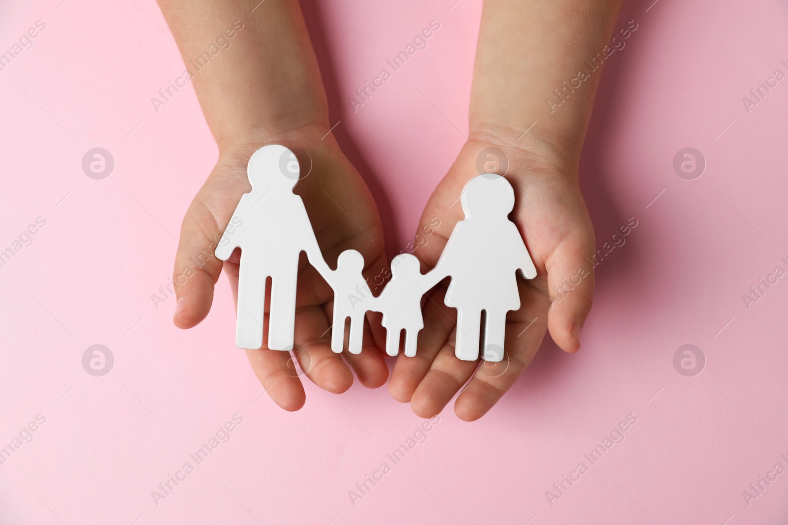 Photo of Child holding figure of family on light pink background, top view