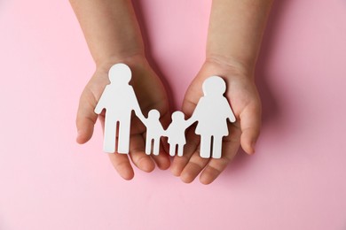 Photo of Child holding figure of family on light pink background, top view