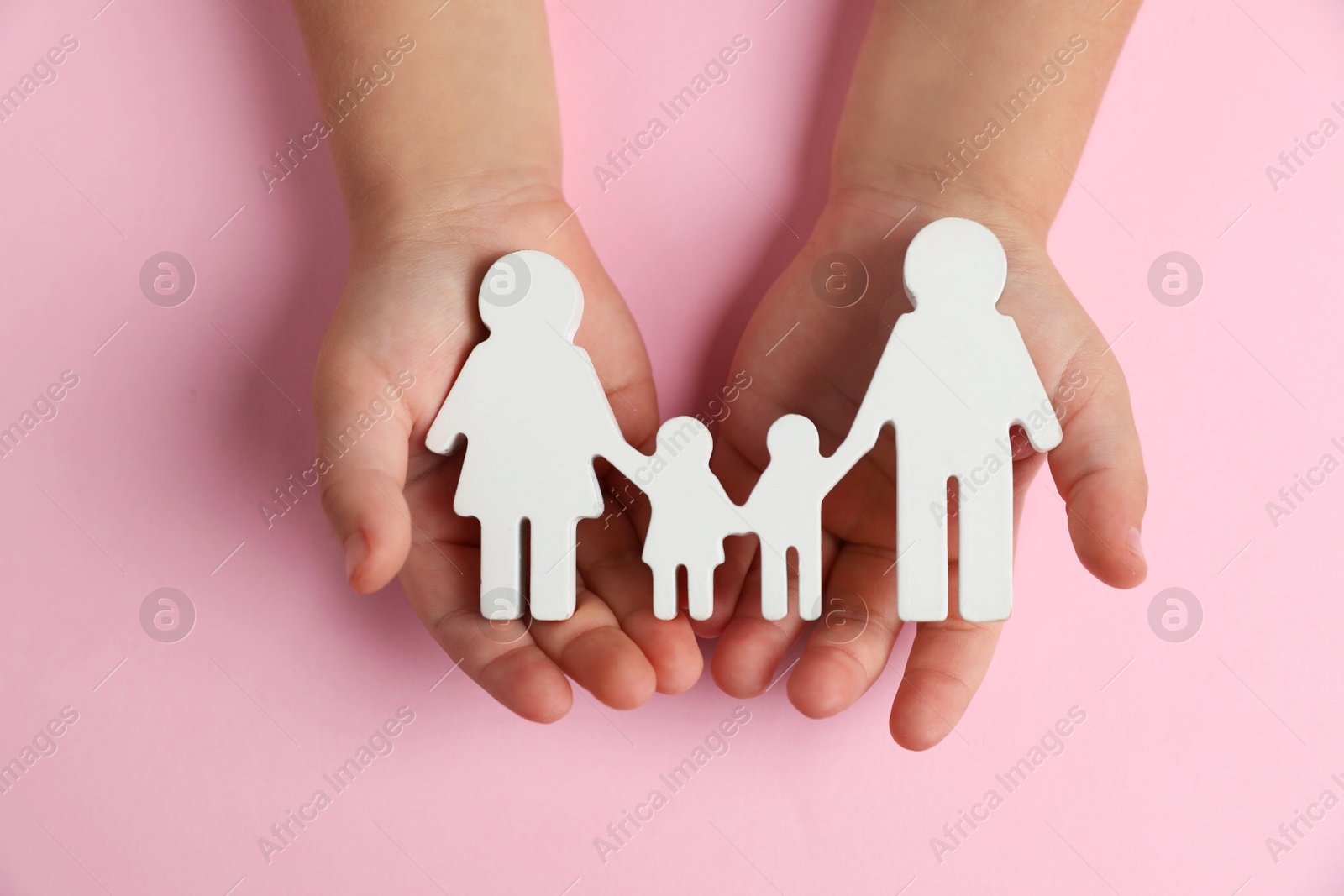 Photo of Child holding figure of family on light pink background, top view