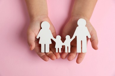 Photo of Child holding figure of family on light pink background, top view