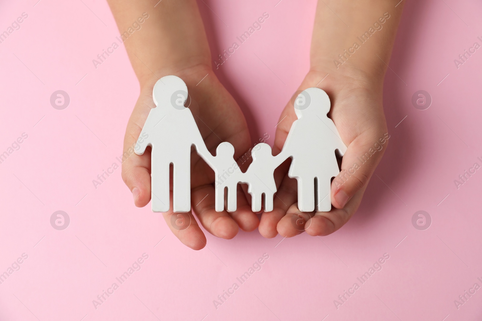 Photo of Child holding figure of family on light pink background, top view