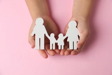 Photo of Child holding figure of family on light pink background, top view