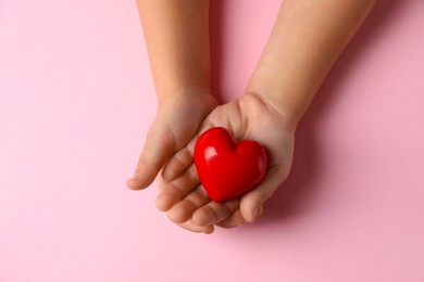 Photo of Child holding decorative red heart on light pink background, top view