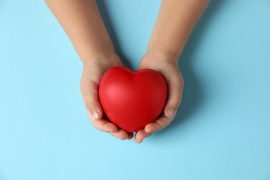 Photo of Child holding decorative red heart on light blue background, top view