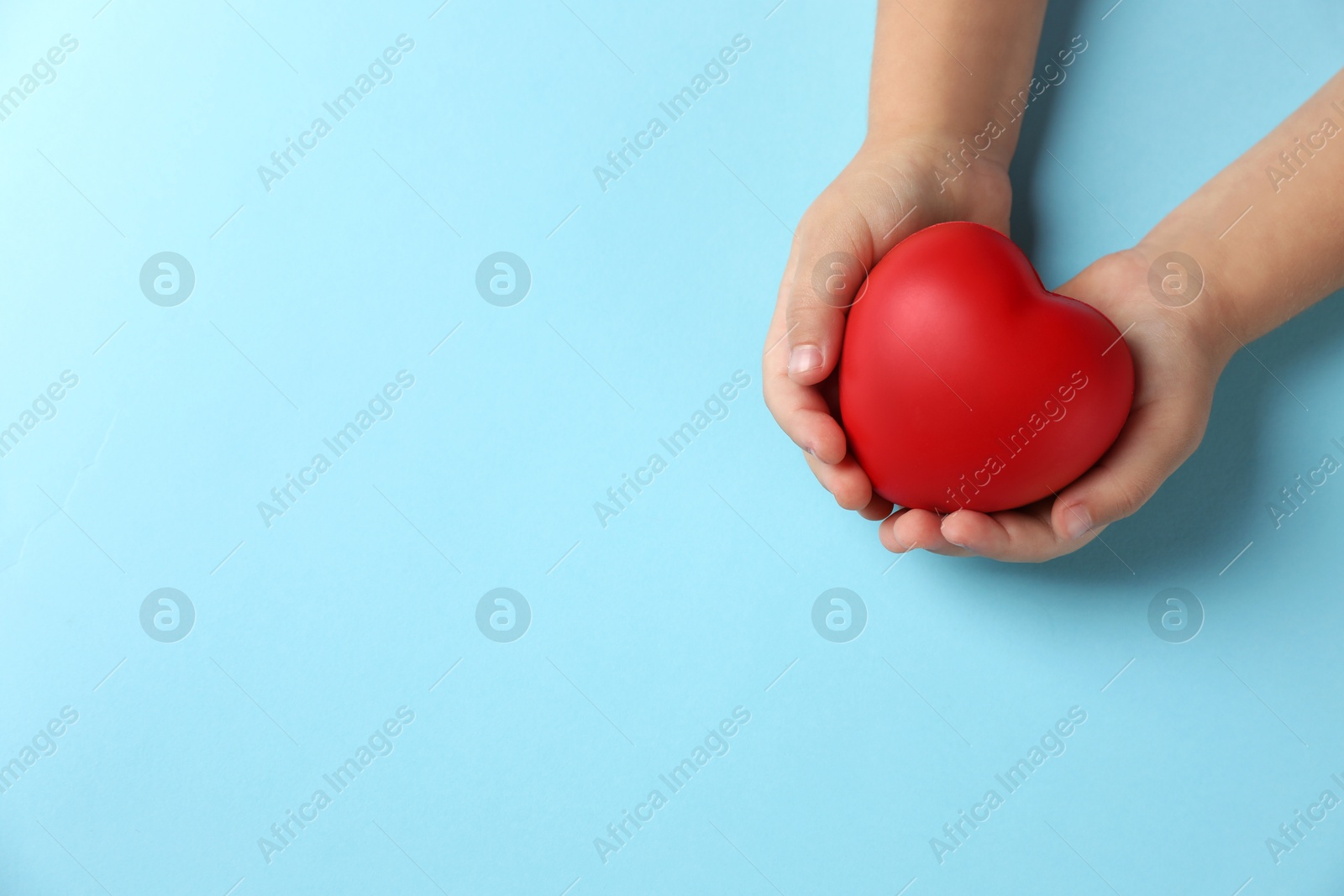 Photo of Child holding decorative red heart on light blue background, top view. Space for text