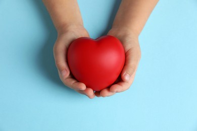 Photo of Child holding decorative red heart on light blue background, top view