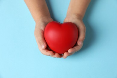 Photo of Child holding decorative red heart on light blue background, top view