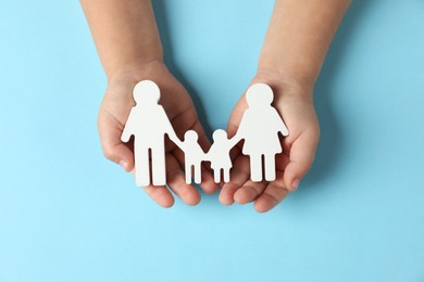 Photo of Child holding figure of family on light blue background, top view