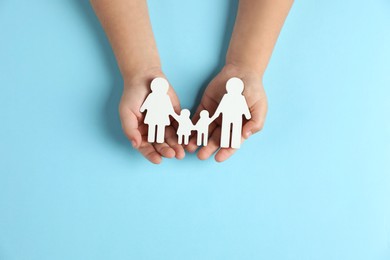 Photo of Child holding figure of family on light blue background, top view