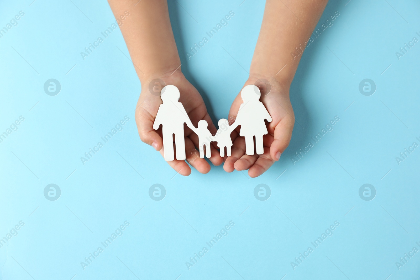 Photo of Child holding figure of family on light blue background, top view