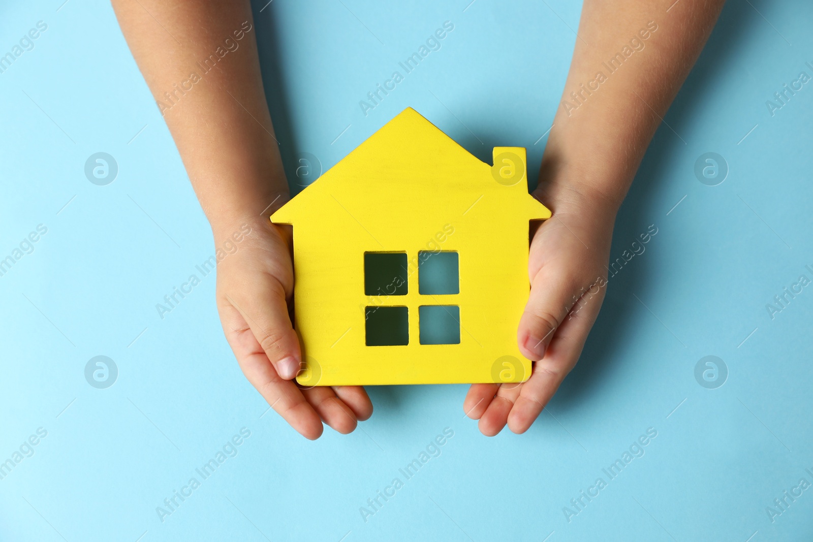 Photo of Child holding house figure on light blue background, top view