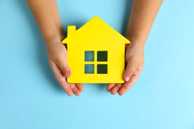 Photo of Child holding house figure on light blue background, top view