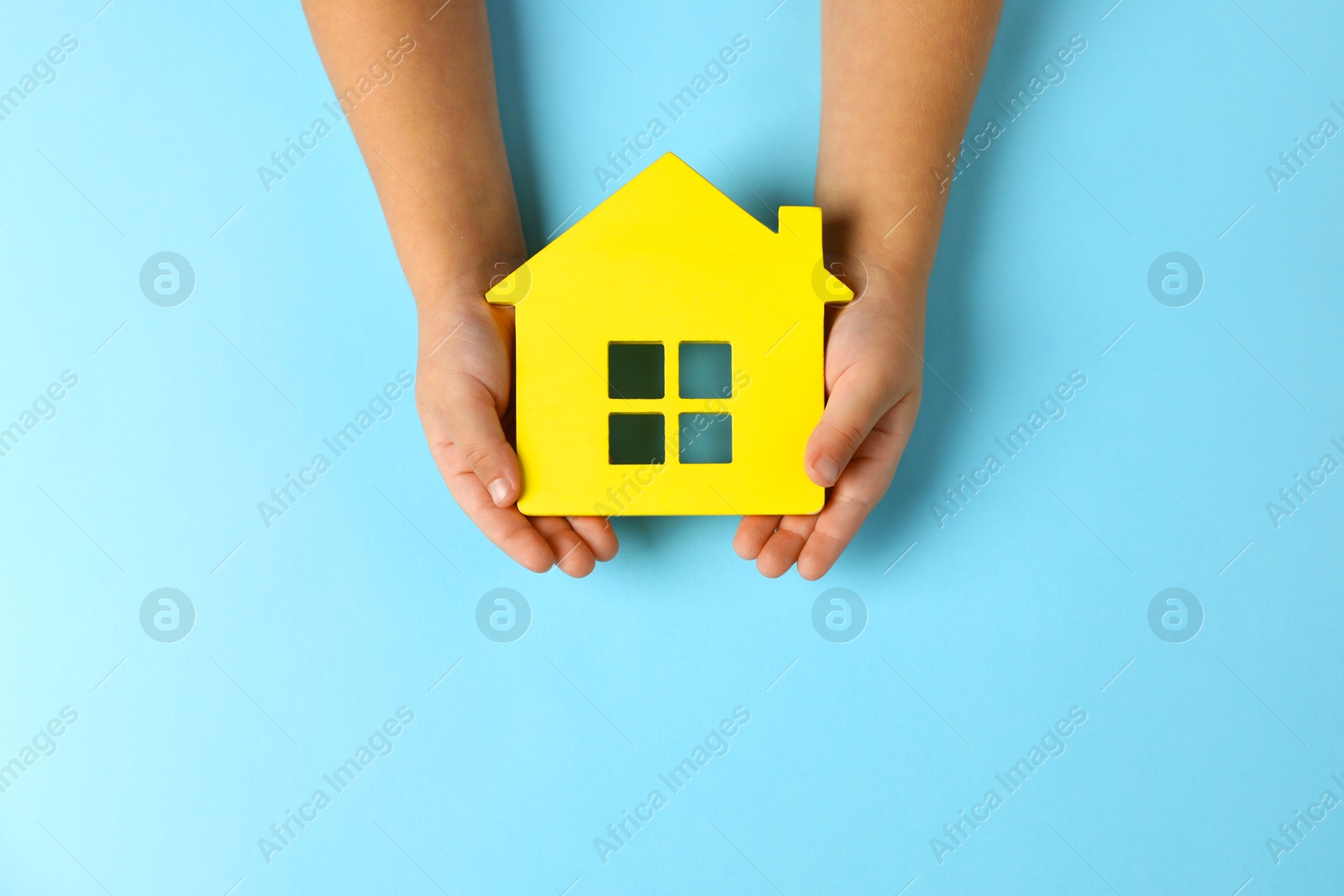 Photo of Child holding house figure on light blue background, top view