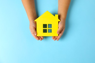 Photo of Child holding house figure on light blue background, top view