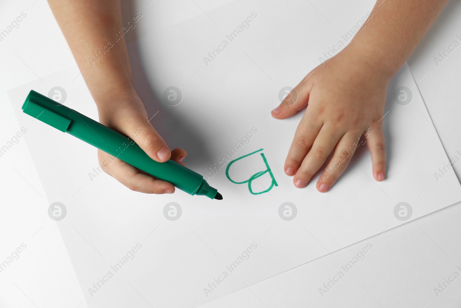 Photo of Little child writing letter B on paper sheet at light table, top view