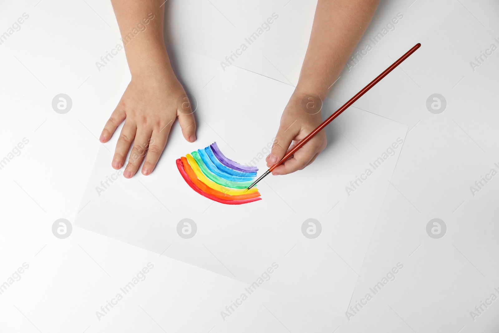 Photo of Little child drawing rainbow with paint at light table, top view