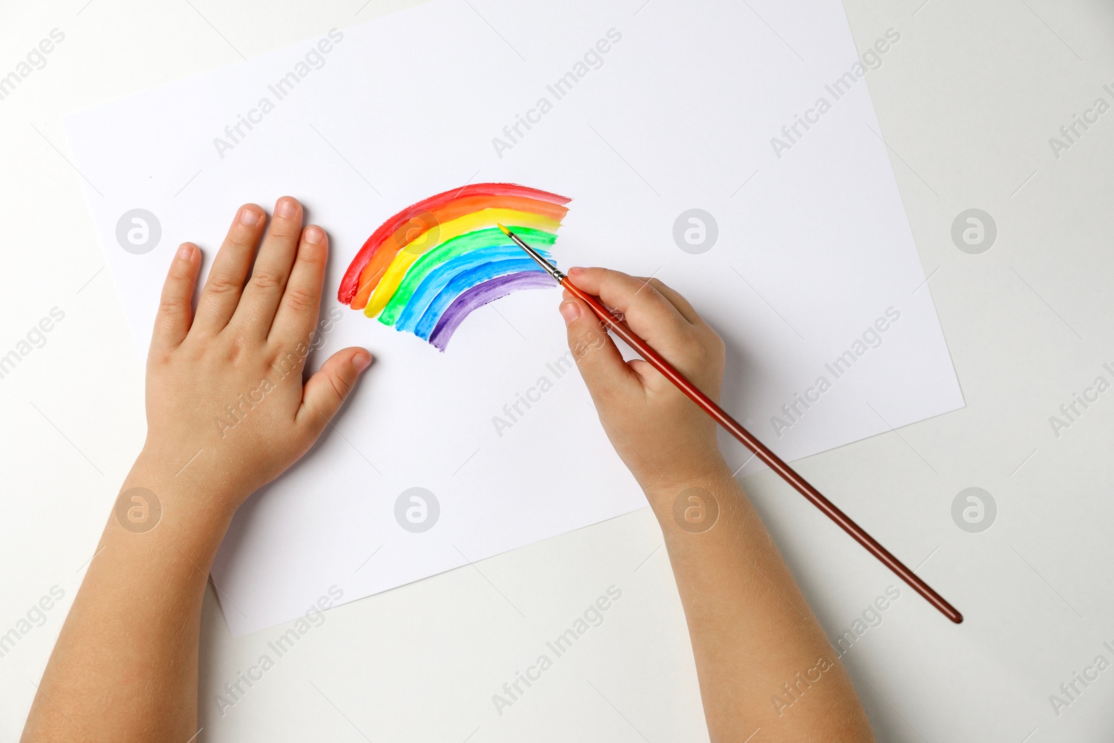 Photo of Little child drawing rainbow with paint at light table, top view