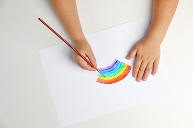 Photo of Little child drawing rainbow with paint at light table, top view