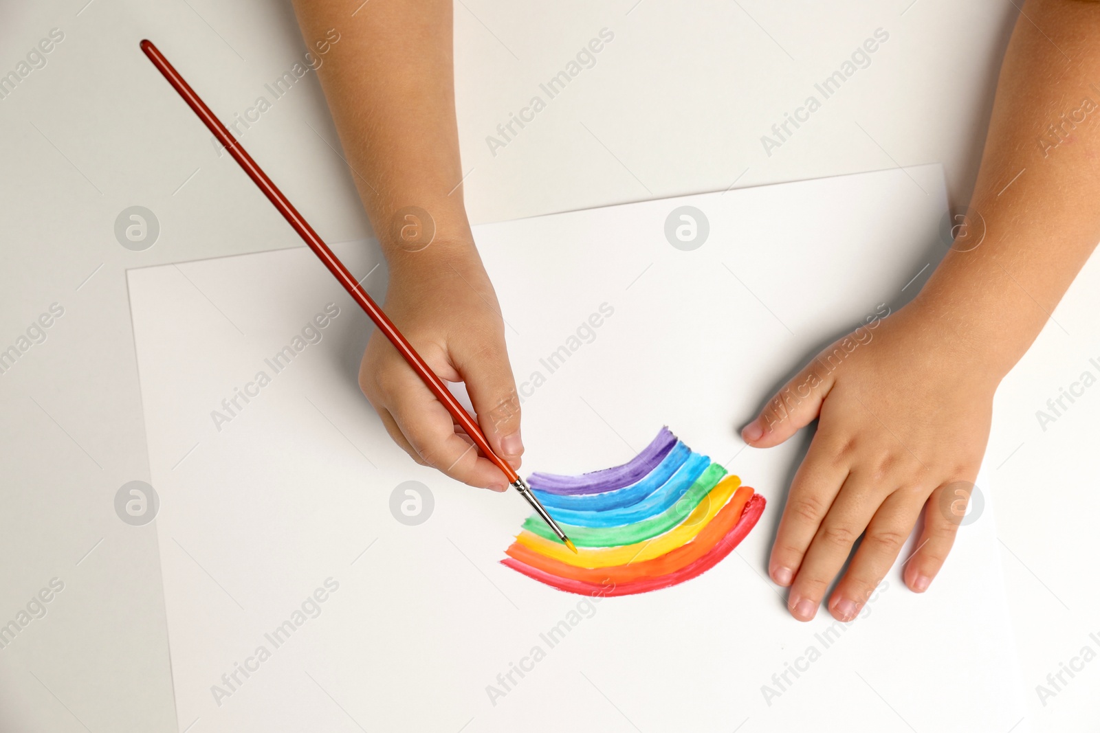 Photo of Little child drawing rainbow with paint at light table, top view