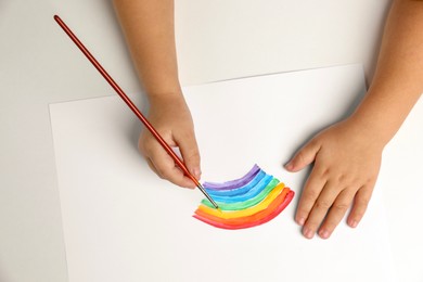 Photo of Little child drawing rainbow with paint at light table, top view