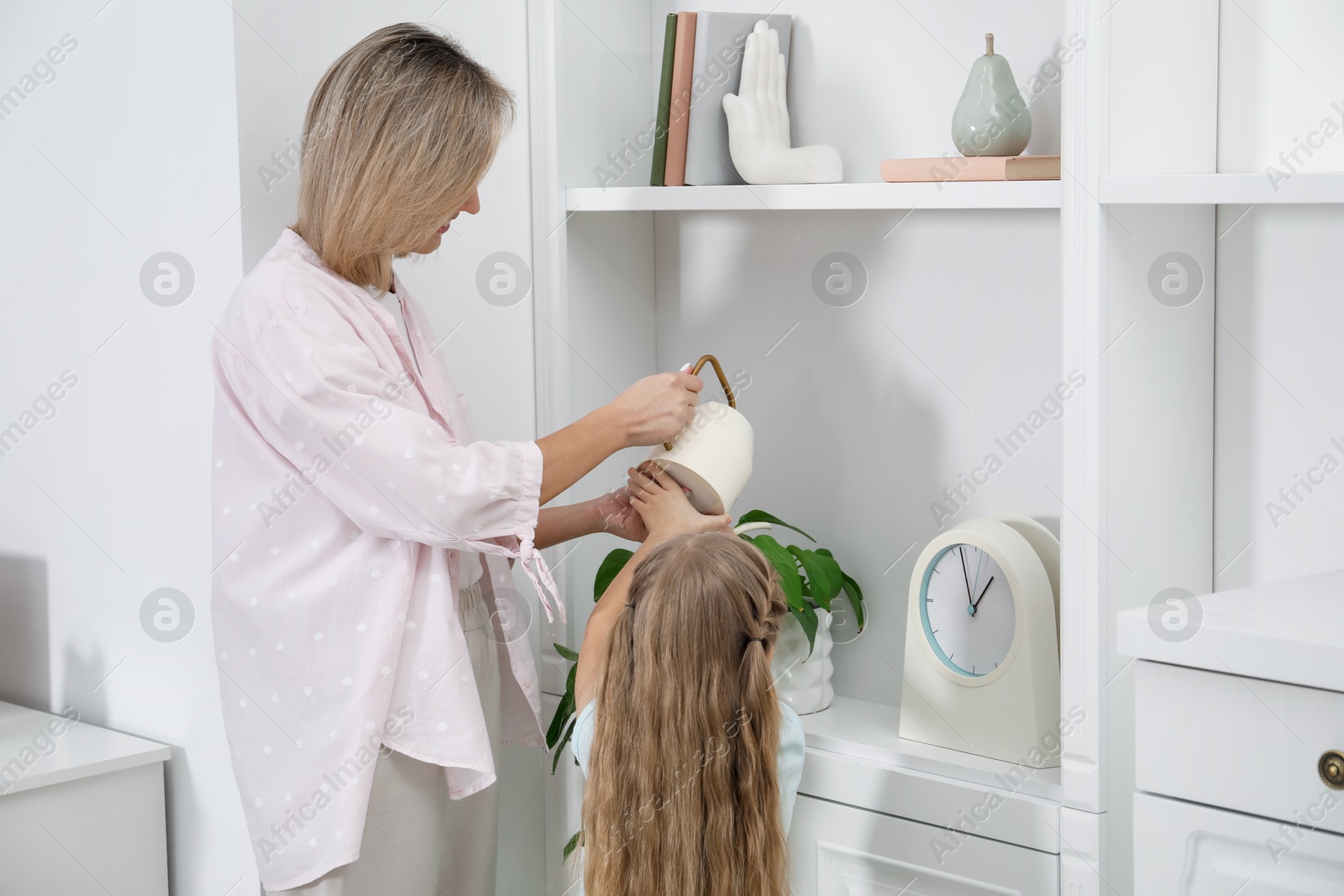 Photo of Little girl helping her mom watering houseplant at home