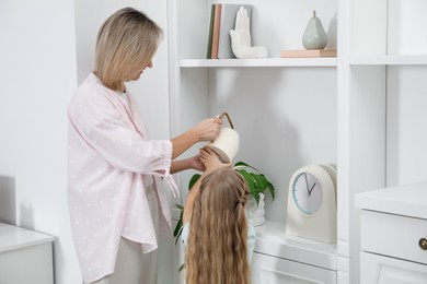 Photo of Little girl helping her mom watering houseplant at home