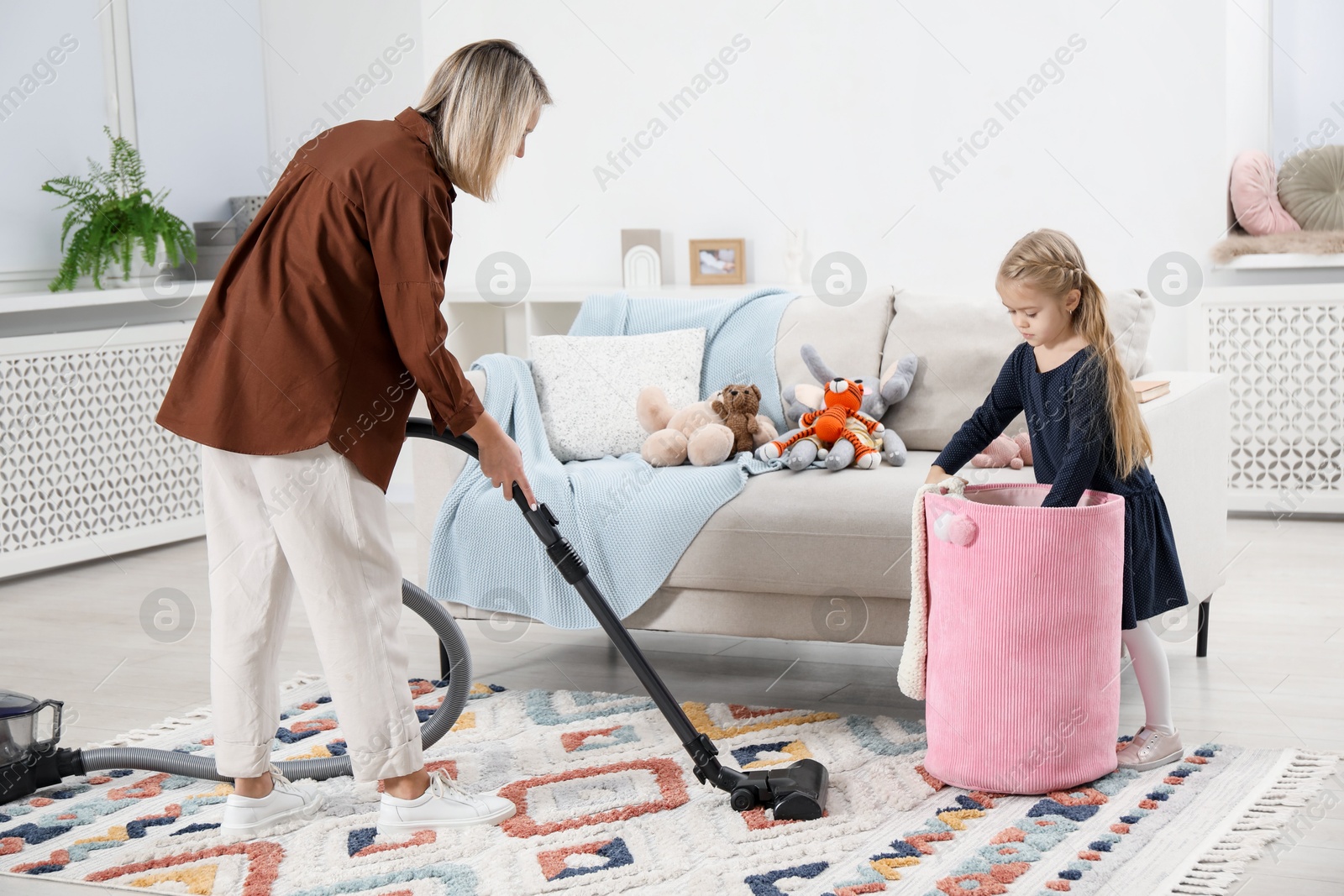 Photo of Little helper. Girl putting away toys while her mother vacuuming at home