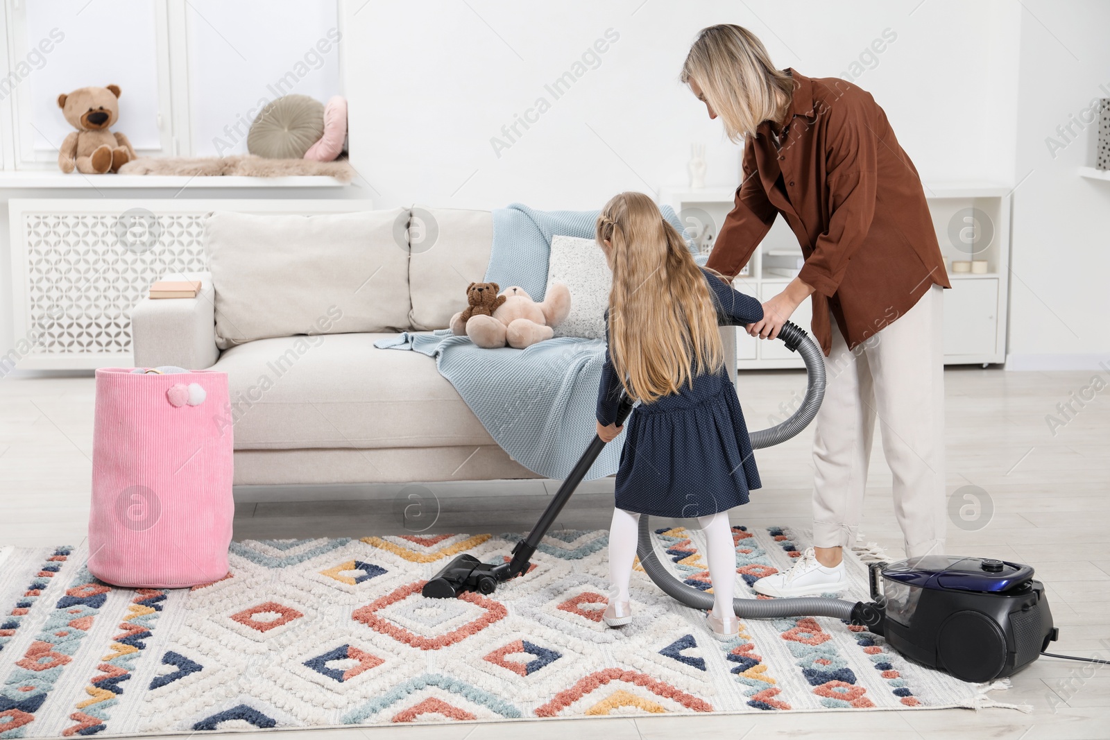 Photo of Little helper. Daughter and mother vacuuming together at home