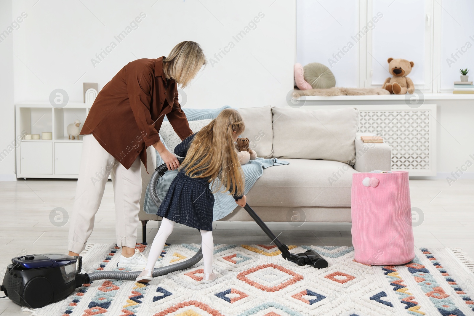 Photo of Little helper. Daughter and mother vacuuming together at home