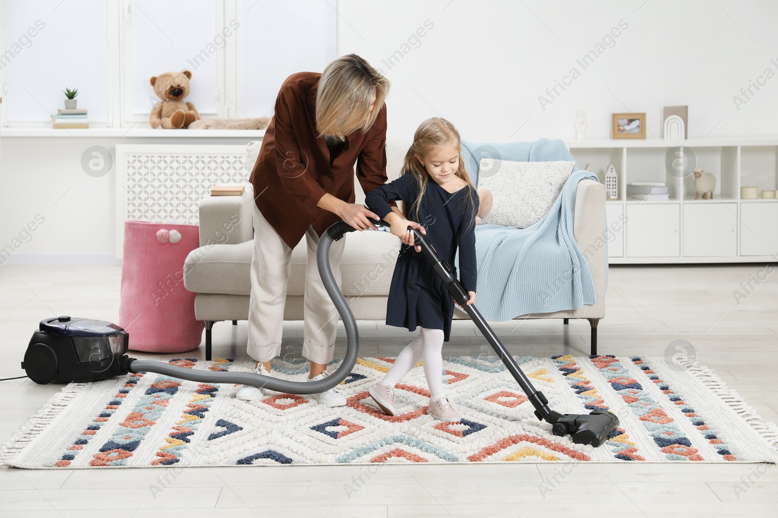 Photo of Little helper. Daughter and mother vacuuming together at home