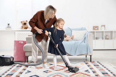 Photo of Little helper. Daughter and mother vacuuming together at home