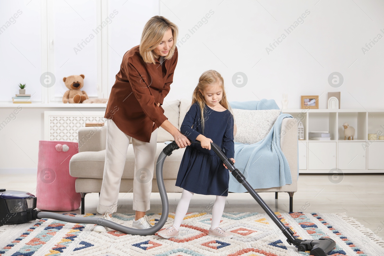 Photo of Little helper. Daughter and mother vacuuming together at home