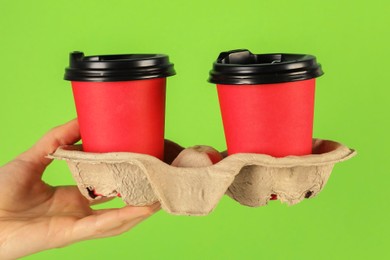 Photo of Woman holding holder with paper cups on green background, closeup. Mockup for design
