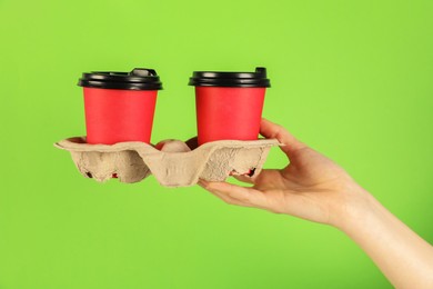 Photo of Woman holding holder with paper cups on green background, closeup. Mockup for design