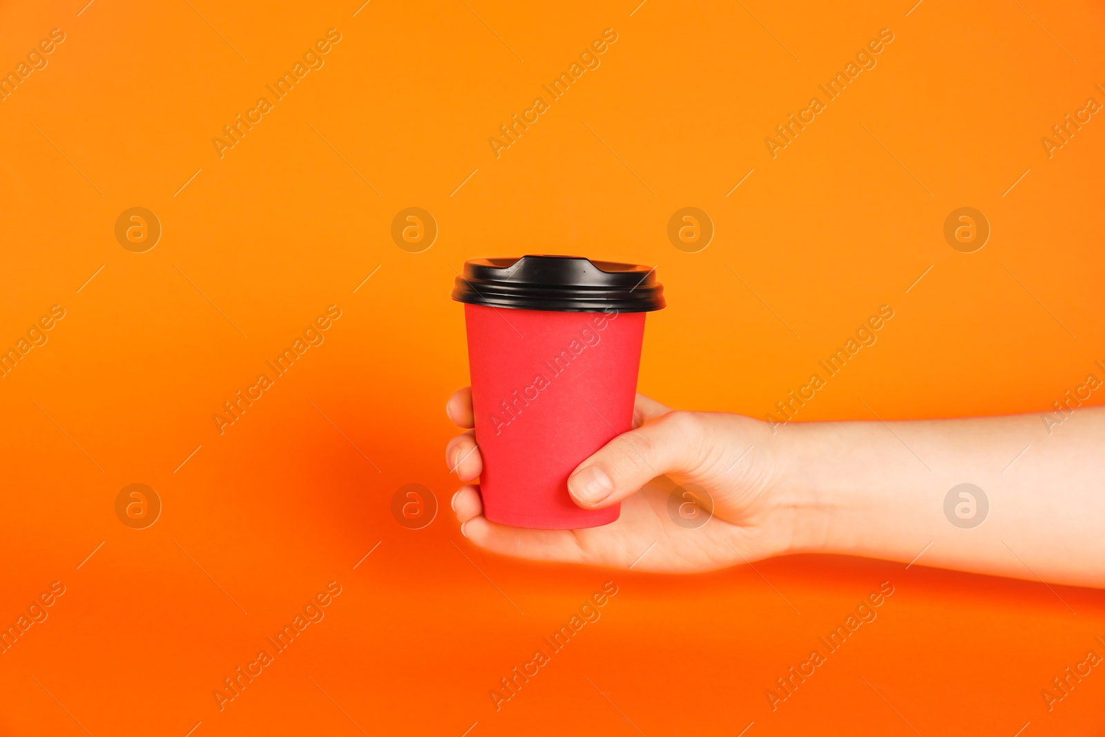 Woman holding paper cup on orange background, closeup. Mockup for design Photo of Woman holding paper cup on orange background, closeup. Mockup for design