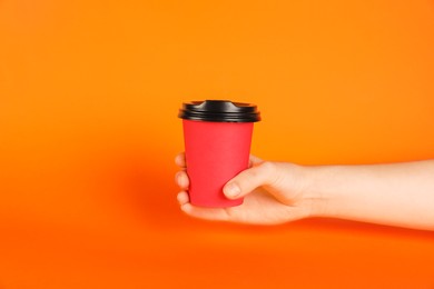 Photo of Woman holding paper cup on orange background, closeup. Mockup for design