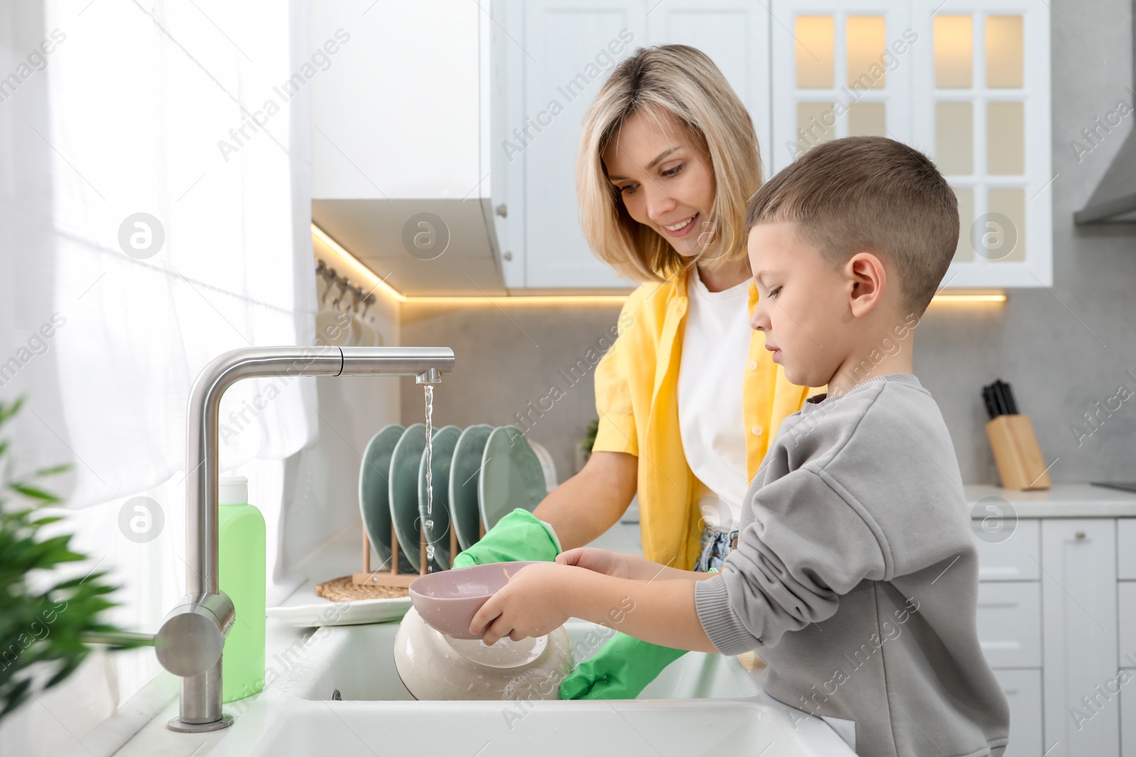 Photo of Little boy helping his mother washing dishes at home