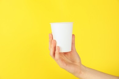 Photo of Woman holding paper cup on yellow background, closeup. Mockup for design