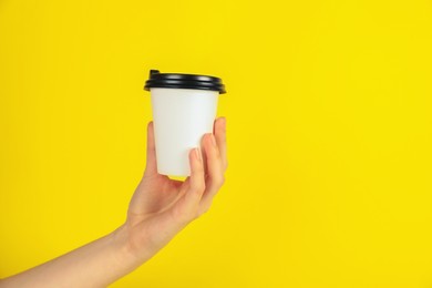 Photo of Woman holding paper cup on yellow background, closeup. Mockup for design