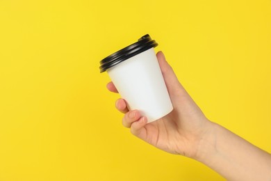Photo of Woman holding paper cup on yellow background, closeup. Mockup for design
