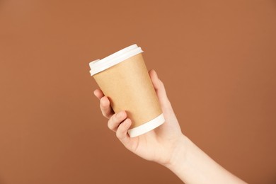 Photo of Woman holding paper cup on brown background, closeup. Mockup for design