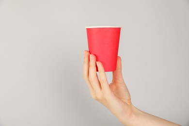 Photo of Woman holding paper cup on grey background, closeup. Mockup for design