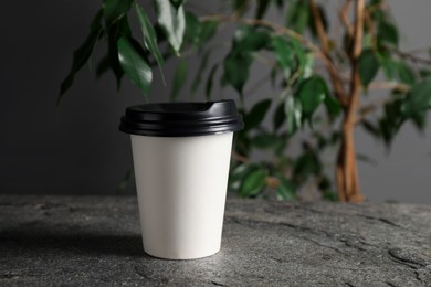 Photo of Paper cup on grey textured table indoors, closeup. Mockup for design