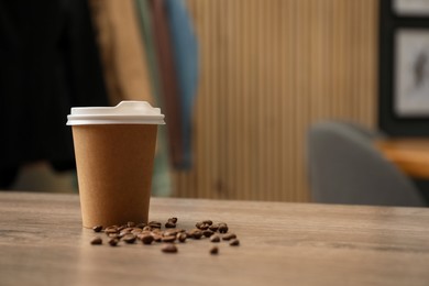 Photo of Paper cup and coffee beans on wooden table indoors. Mockup for design