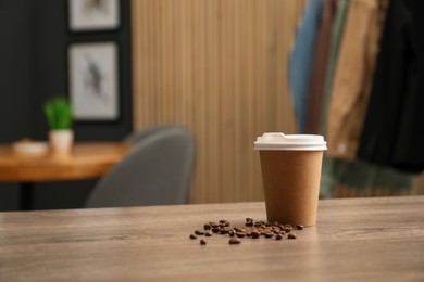 Photo of Paper cup and coffee beans on wooden table indoors. Mockup for design