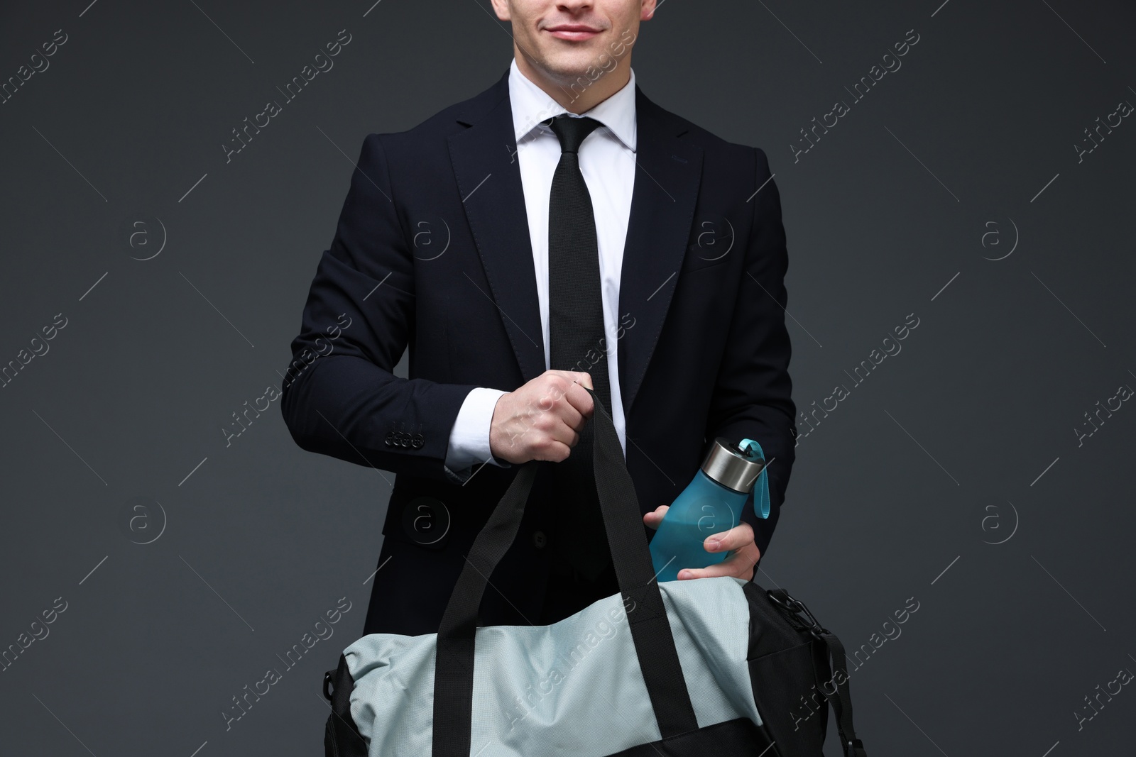 Photo of Man in suit putting bottle of water into gym bag on dark grey background, closeup