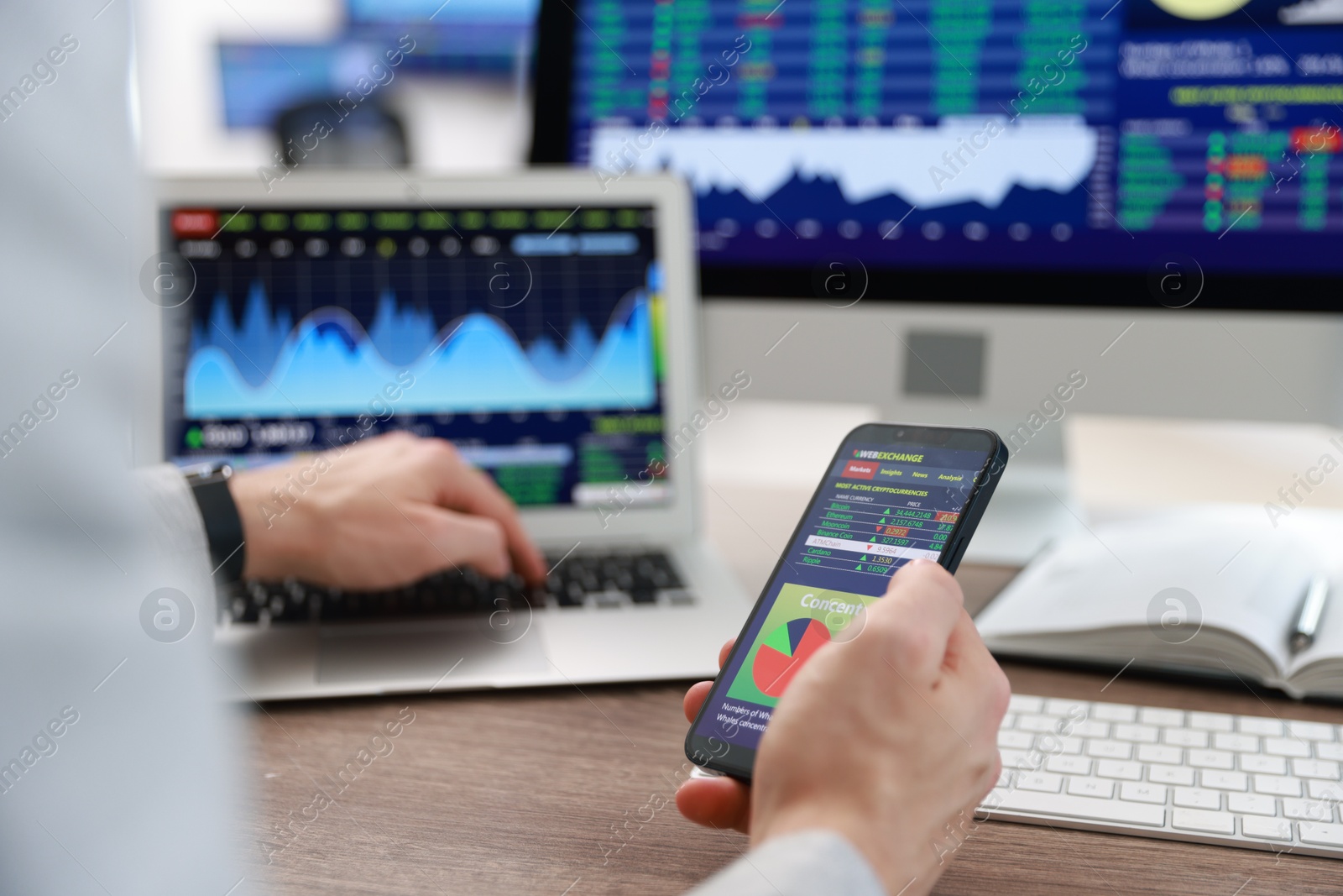 Photo of Financial trading specialist with smartphone and laptop at table in office, closeup